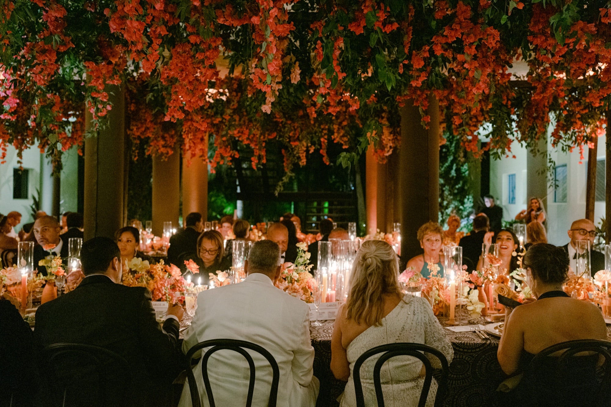 A long candlelit table beneath hanging bougainvillea at night